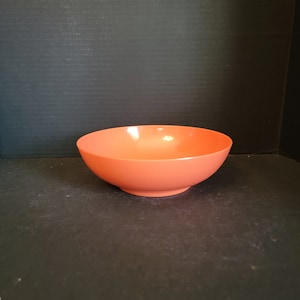 May include: A large, round, orange-colored bowl made of plastic. The bowl is sitting on a black surface.