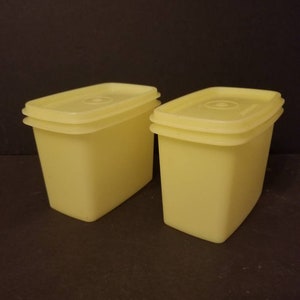 May include: Two yellow plastic rectangular storage containers with lids. The containers are stacked on top of each other.