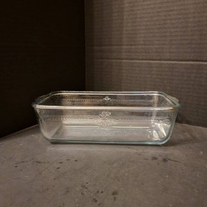 May include: A clear glass loaf pan with a decorative pattern around the rim.