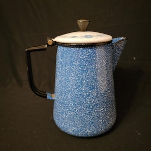 May include: A blue speckled enamelware coffee pot with a black handle and spout. The lid is white with a floral design and a black knob. This vintage kitchenware item is perfect for camping or home use.