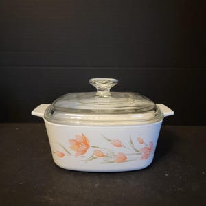 May include: A white square casserole dish with a glass lid. The dish has a floral design with pink flowers and green leaves.