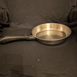 May include: A stainless steel frying pan with a black handle. The pan is round with a slightly curved edge and a long handle for easy use. The pan is designed for cooking.