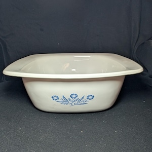 May include: A white, rectangular serving bowl with a flared rim. The bowl features a blue floral design on the front. The bowl is made of a durable material and is suitable for serving various dishes.