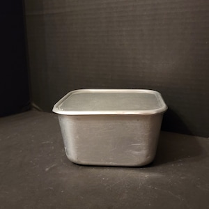 May include: A silver square-shaped metal container with a lid. The container has a smooth, slightly textured surface.