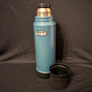 May include: A teal Stanley Sport thermos with a black cap and cup. The thermos has a silver top and a textured finish. The Stanley Sport logo is visible on the front. The cup is next to the thermos.