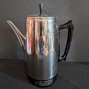 May include: A stainless steel Hamilton Beach coffee maker with a black handle and lid. The coffee pot has a spout and a black base with the text "Stainless Steel" and "Hamilton Beach 10 Cup".