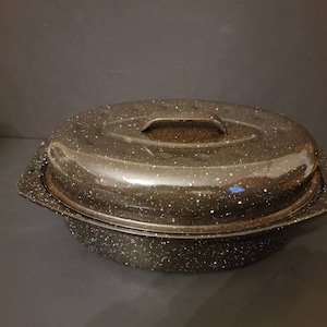 May include: Oval-shaped, speckled black roasting pan with a matching lid. The pan has a handle on the lid and side handles for easy transport. The speckled pattern is white against the black enamel. A kitchenware item.