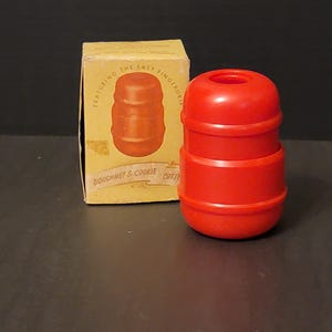 May include: A bright red plastic doughnut and cookie cutter with a cylindrical shape. The cutter is next to a vintage box with the text "Featuring the Easy Fingergrip" and an illustration of the cutter. The box is tan with red text.