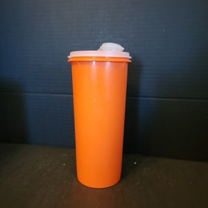 May include: An orange plastic tumbler with a white and pink lid. The tumbler is cylindrical and has a smooth surface. The lid has a flip-top opening. The background is a dark blue-gray.