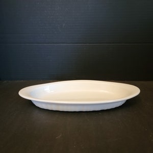 May include: A white oval serving dish with a fluted rim. The dish is made of ceramic or porcelain and is empty. The dish is on a dark surface.