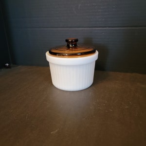 May include: A white ceramic jar with a brown glass lid. The jar has a ribbed design and the lid has a knob on top.
