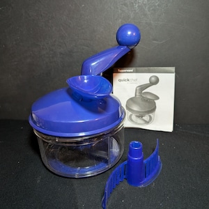 May include: A blue and clear plastic Tupperware Quick Chef food chopper with a manual handle and blade attachment. The product includes a clear container, a blue lid, and a small instruction booklet.