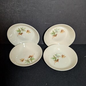 May include: Four off-white ceramic bowls with a leaf design in green, brown, and yellow. The bowls are oval-shaped and have a shallow depth. The leaf design is centered on each bowl, with a dark background.