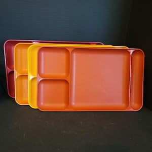 May include: A stack of colorful divided trays in shades of red, yellow, and orange. Each tray has multiple compartments for separating food items. The trays are made of plastic and are designed for easy cleaning and use.