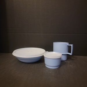May include: A set of three blue plastic containers with lids. The set includes a bowl, a small container, and a mug.