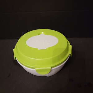 May include: A white and green round food storage container with a lid. The lid is green with a white oval-shaped section in the center. The container has two green clips on the sides to secure the lid. The text "WENT KITCHEN" is printed on the lid.
