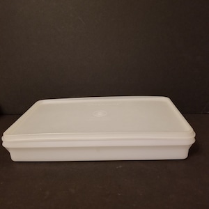 May include: A rectangular, white plastic food storage container with a matching lid. The container has a simple, clean design, with a slightly raised edge on the lid and a smooth, matte finish. The container is empty.