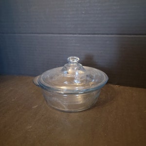 May include: A clear glass butter dish with a lid. The dish has a decorative pattern around the rim.