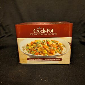 May include: A rectangular Crock-Pot recipe card collection box. The box is primarily red with a white panel displaying a bowl of food. Text on the box reads "Crock-Pot Recipe Card Collection" and "The Original and #1 Brand Slow Cooker."