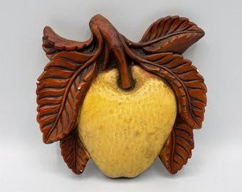 May include: A wooden wall decor piece shaped like an apple with brown leaves. The apple is yellow and has a textured surface.