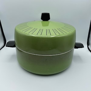 May include: A green metal pot with a black knob on the lid. The pot has a white rim and black lines around the top.