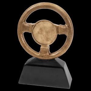 May include: A bronze-colored steering wheel trophy with a textured grip and a circular center, mounted on a black, trapezoidal base. The trophy is designed to resemble a classic car steering wheel.