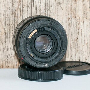 May include: A black camera lens with a silver ring around the lens. The lens is sitting on a black lens cap.