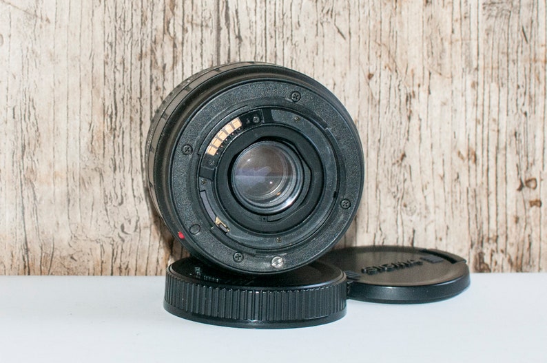May include: A black camera lens with a silver ring around the lens. The lens is sitting on a black lens cap.