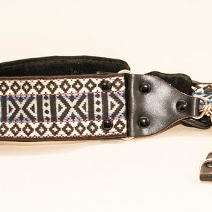 Op de afbeelding: Een zwart-wit gepatenteerde cameraband met een zwart lederen gedeelte en zilveren metalen clips.