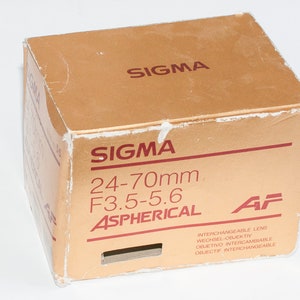 May include: A gold box with the text "SIGMA 24-70mm F3.5-5.6 ASPHERICAL AF" printed on it. The box is for an interchangeable lens.