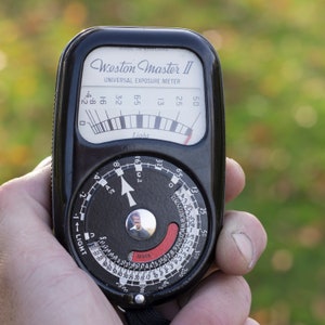 May include: A black Weston Master II Universal Exposure Meter with a silver needle and a black and red dial. The meter has a light reading scale and a film speed setting dial.