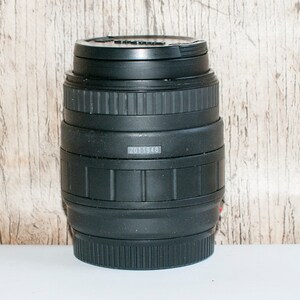 May include: Black camera lens with a silver band and the number 2011948 printed on it.