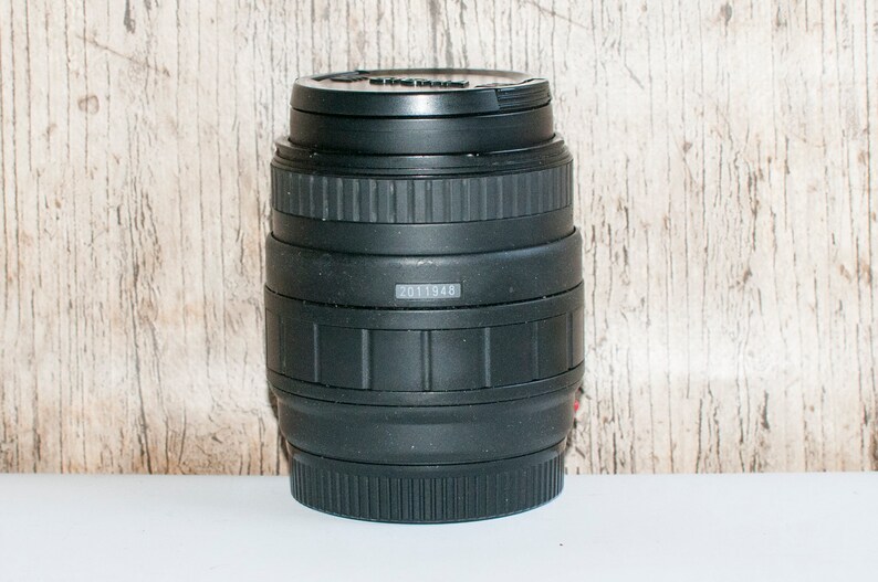 May include: Black camera lens with a silver band and the number 2011948 printed on it.