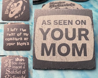 May include: A collection of slate coasters with various engraved designs and text. One coaster reads "AS SEEN ON YOUR MOM." Other coasters feature phrases like "Fun Science Fact: Uranus" and "I left the rest of my coasters at your Mom's."