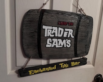 May include: A wooden barrel sign with the text "Ship to Trader Sam's Enchanted Tiki Bar" in white and yellow lettering. The barrel is painted gray and has a wood grain texture.