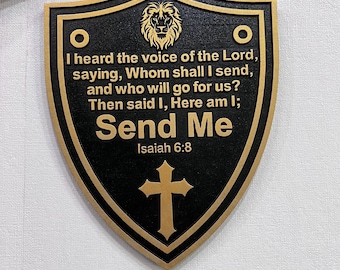 May include: A black and gold shield-shaped plaque with the text "I heard the voice of the Lord...Send Me Isaiah 6:8". The plaque features a lion's head, a cross, and two circles. The design is carved into the surface.