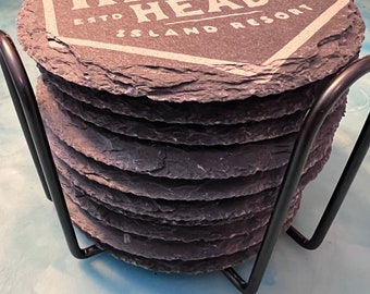 May include: A set of six black slate coasters with a white logo that reads "Disney's Hilton Head Island Resort Est. 1996". The coasters are stacked in a black metal holder.