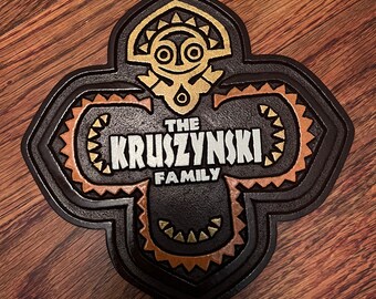 May include: A brown wooden sign with a gold and orange tiki-style design. The sign says "The Kruszynski Family" in white letters.