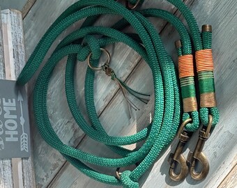 May include: Emerald green dog leash with bronze-colored hardware. The leash is made of a thick, braided rope and features a loop handle, a metal ring, and a decorative tassel. The leash has a matching collar with orange and green accents.