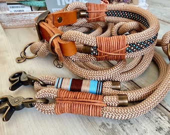 Op de afbeelding: Hondenhalsband en -riem set van beige touw met bruin lederen accenten en metalen hardware. De halsband heeft een vredesteken bedel. De riem heeft een bruin, blauw en wit gestreept accent. Voor huisdieren.