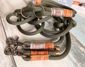 May include: Olive green rope dog leash and collar set. The leash and collar are made of thick, braided rope with bronze-colored metal hardware. The rope is accented with tan and orange thread wrapping.