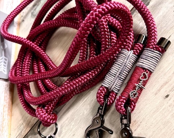 May include: A burgundy dog leash made of thick, braided rope. The leash has two black metal clasps and decorative silver and white accents. One leash end has a paw print charm and a heart charm.