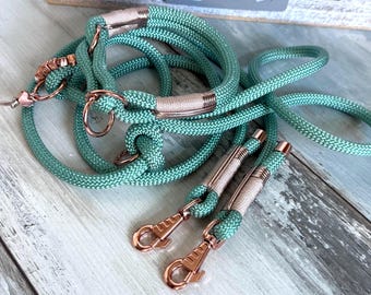May include: A teal dog leash and matching collar set with rose gold-colored hardware. The rope-style leash and collar have a woven texture. The set includes a leash with a clasp and a collar with a metal ring.