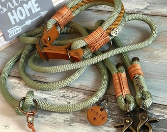 May include: A dog collar and leash set in shades of green and brown. The collar and leash are made of a thick, woven rope material. The collar features brown leather accents and a metal buckle. The leash has metal clasps and a matching leather accent. A small tag is included.