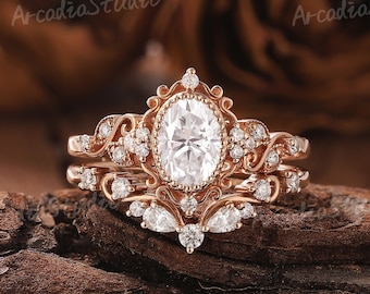 May include: A rose gold engagement ring set with an oval-shaped center stone and smaller accent stones. The ring is set in a delicate, ornate design.