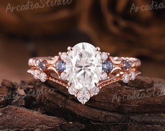 Puede incluir: Conjunto de anillo de compromiso de oro rosa con una piedra central de corte ovalado y piedras redondas más pequeñas. La banda presenta un delicado diseño trenzado con piedras de acento azules.