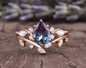 May include: A pear-shaped blue and purple gemstone engagement ring set with a delicate, leaf-shaped band. The ring is set in rose gold and features a cluster of small diamonds.