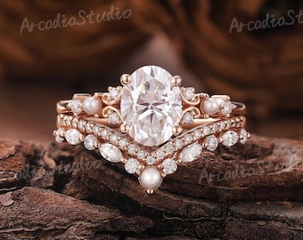 May include: A rose gold engagement ring set with a large oval-shaped center stone and smaller round stones. The ring is accented with pearls and has a delicate, vintage-inspired design.
