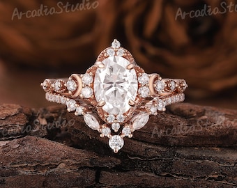 Puede incluir: Un anillo de compromiso de oro rosa con una piedra central ovalada grande y piedras redondas más pequeñas. El anillo está colocado sobre una superficie de madera.