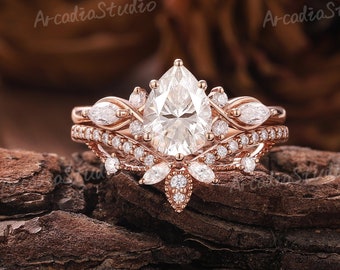 Puede incluir: Un anillo de compromiso de diamante de forma pera engastado en oro rosa con un delicado diseño floral. El anillo presenta una piedra central de forma pera rodeada de diamantes más pequeños y detalles florales intrincados. La banda también está engastada con diamantes más pequeños.